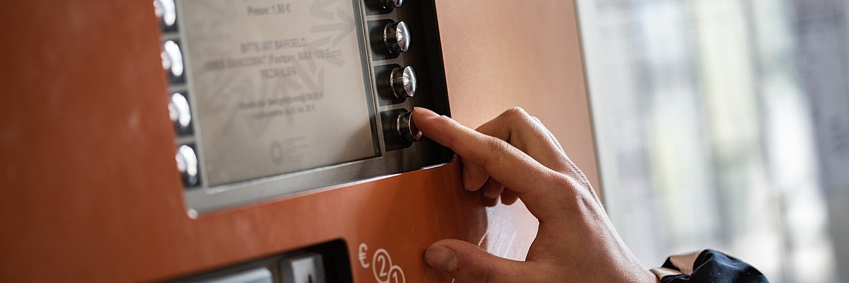 Particolare della mano di una persona intenta a scegliere un'opzione a lato dello schermo di una biglietteria automatica.